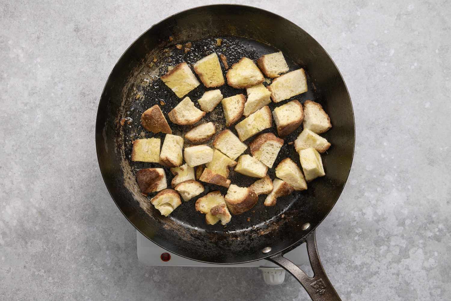 A large skillet with chunks of sourdough bread toasting in olive oil