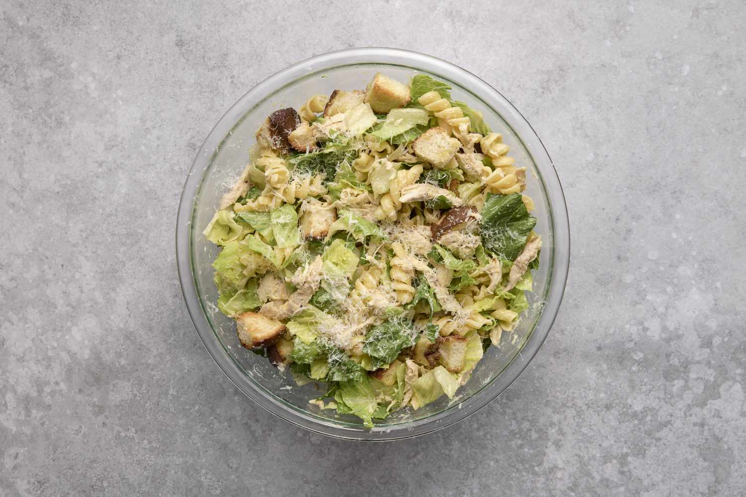 A bowl of chicken caesar pasta salad with rotissere chicken, fusilli pasta, romaine lettuce, and topped with Parmigiano-Reggiano