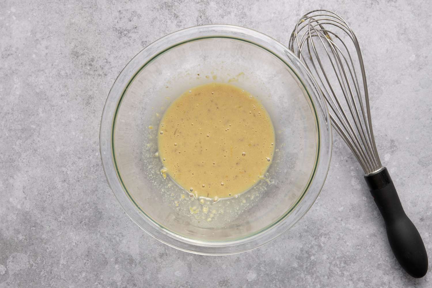 A bowl of lemon juice and zest, egg yolk, and dijon mustard with a whisk
