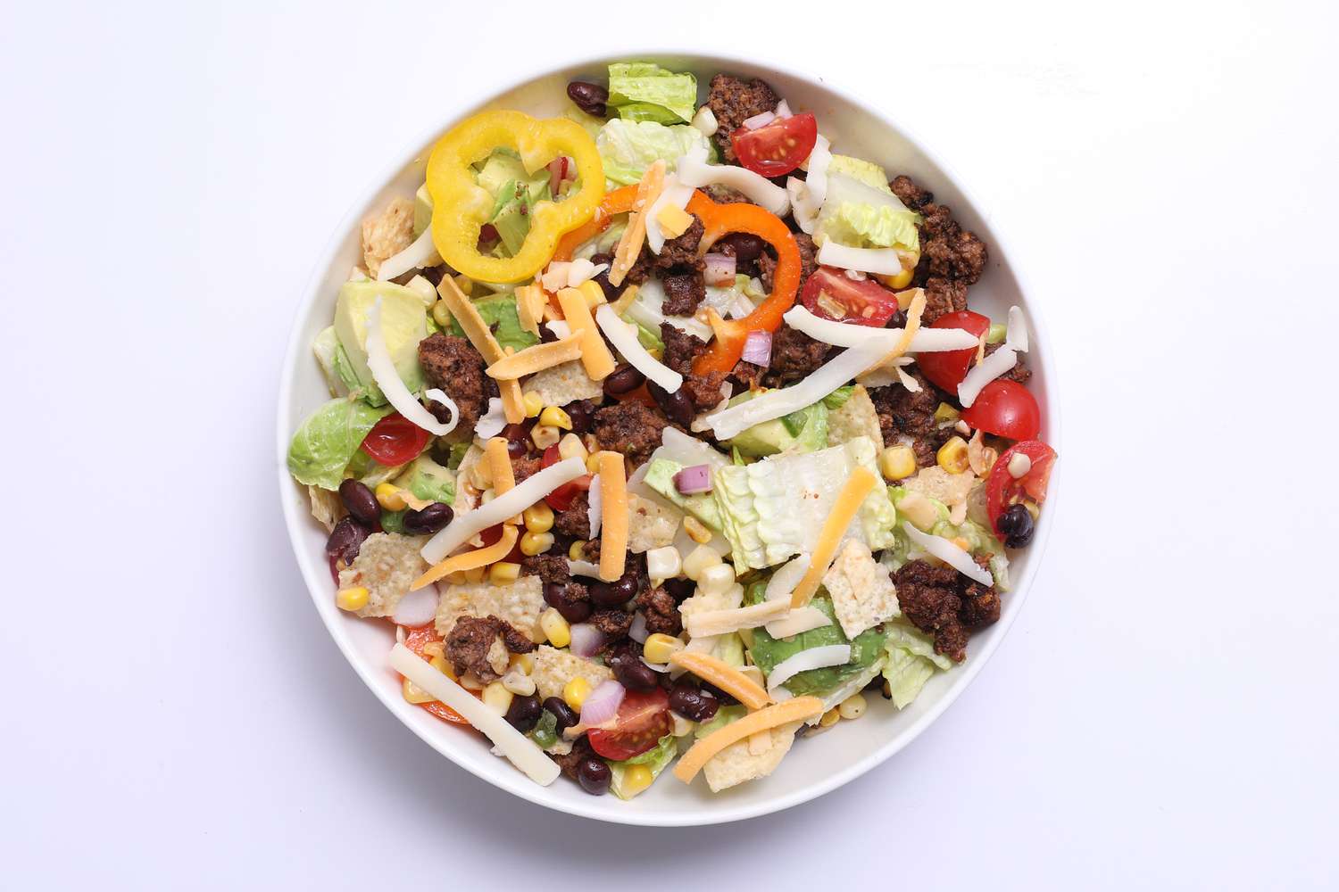 A bowl of taco salad showing romaine lettuce, ground beef, peppers, cherry tomatoes, and shredded cheese