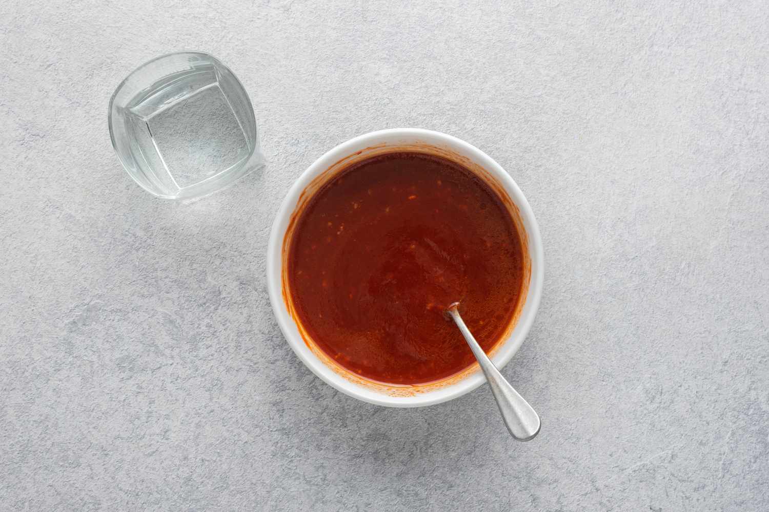 Korean dipping sauce in a bowl and a glass of water to the side