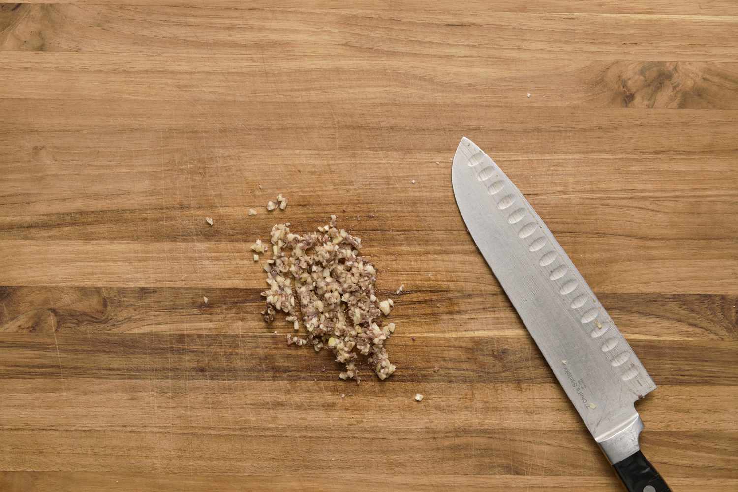 A pasta of anchovies, garlic, and salt on a cutting board next to a knife
