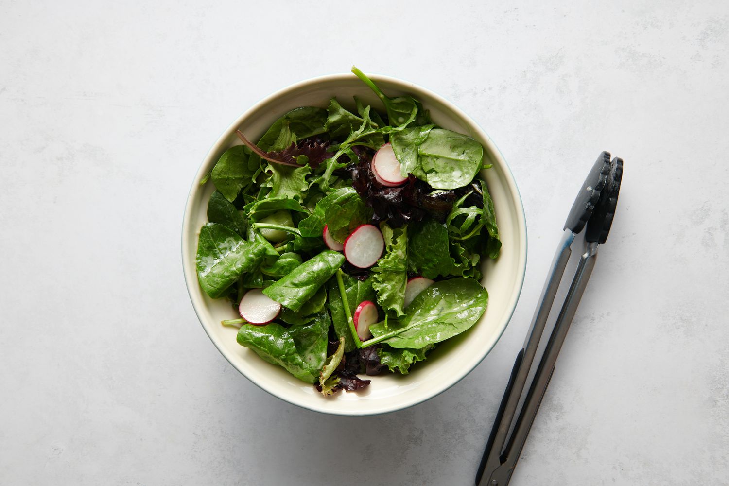 A bowl of spring mix, arugula, radishes, and cucumbers dressed with a lemon vinaigrette